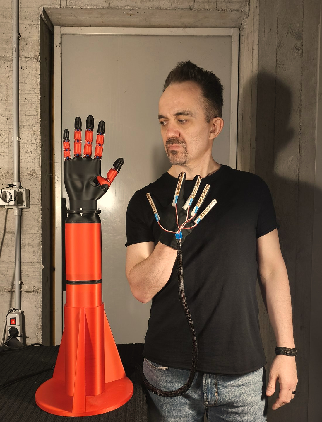 Andrea Milani nel suo laboratorio, con il guanto di sensori di flessione alla mano e la mano teleoperata stampata in 3D accanto a lui.