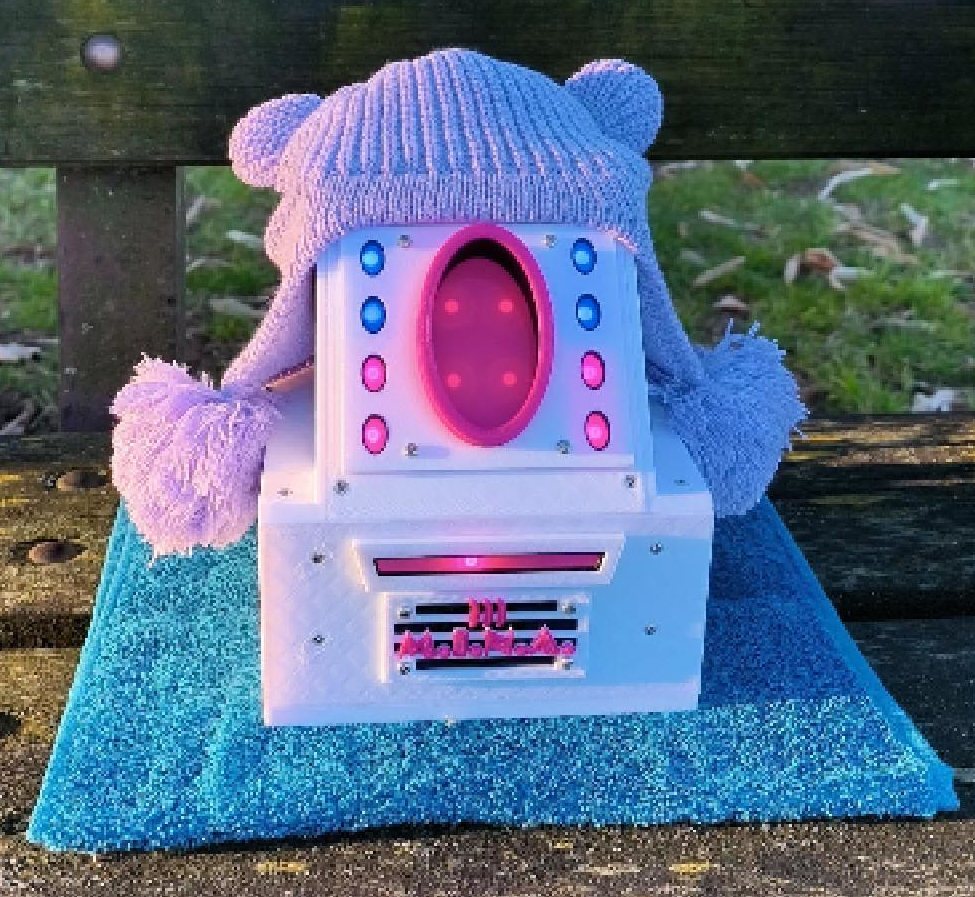 M.I.N.A., dispositivo stampato in 3D bianco con LED rosa e azzurri, indossa un berretto di lana lilla con pon pon ed &egrave; appoggiata su una panchina.